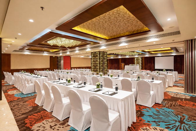 Grandeur banquet hall in Nashik with elegant round tables, floral 
centerpieces, dining setup, decorated stage and spacious event space