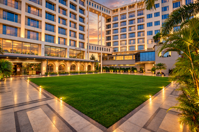 Lush outdoor event lawn in Nashik with landscaped greenery, hotel backdrop, paved walkways and evening lighting